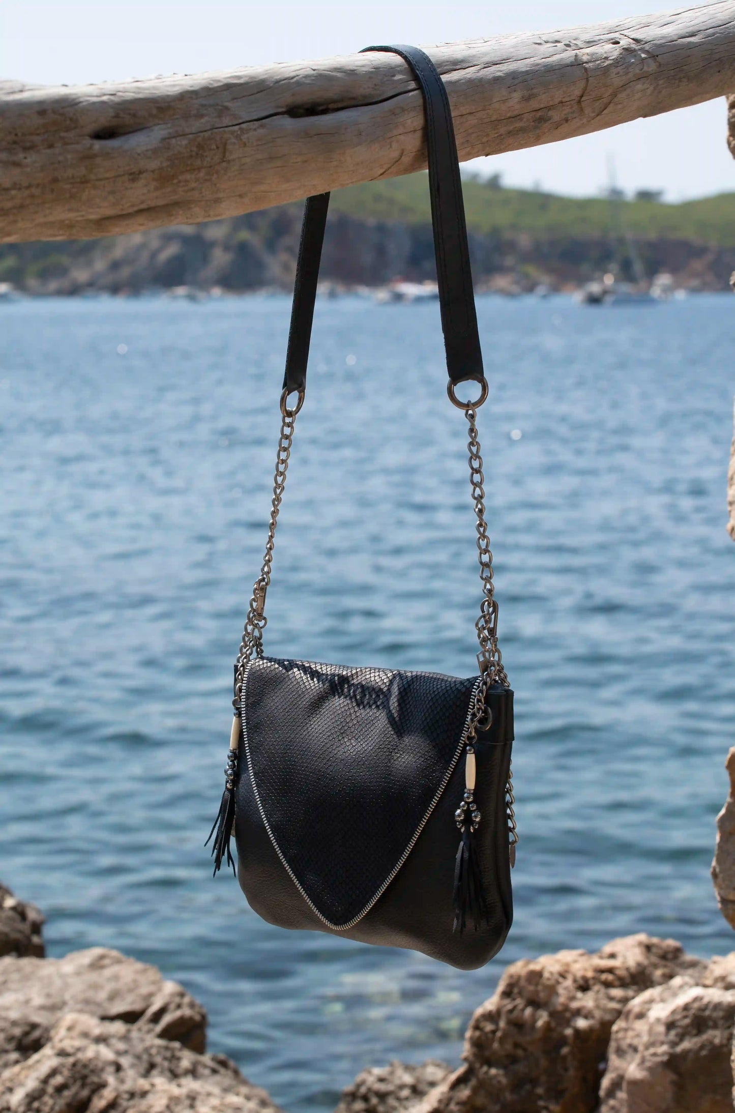 Woman wearing an artisanal black leather bag with silver chain strap and unique snake texture, a sophisticated boho-chic accessory handmade in Ibiza.