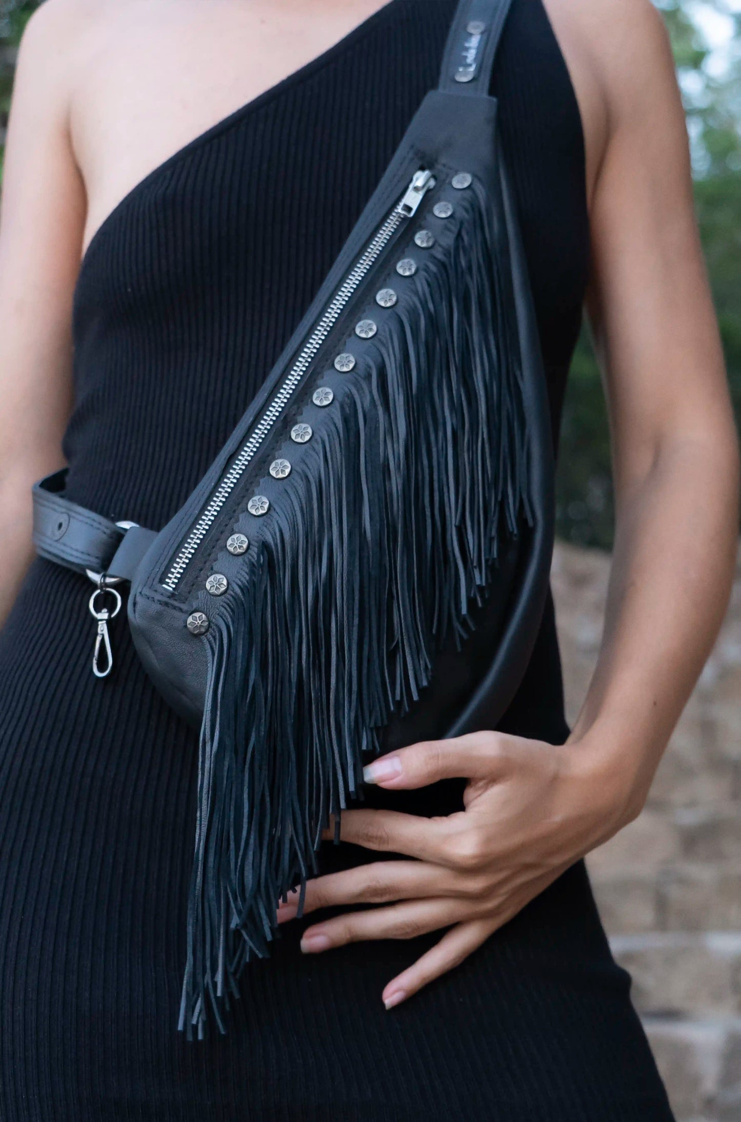 Woman wearing a premium black leather sling bag with long fringes, a bohemian artisan accessory handmade in Ibiza.
